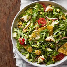 a salad with chicken, tomatoes and lettuce in a white bowl on top of a wooden table