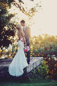 a bride and groom standing on a stone wall