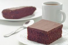 a piece of chocolate cake on a plate with a cup of coffee in the background