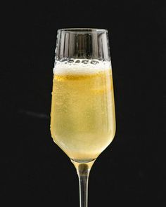 a wine glass filled with liquid on top of a table next to a black background