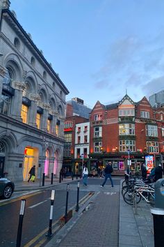 people are walking down the street in front of some buildings and shops at dusk time