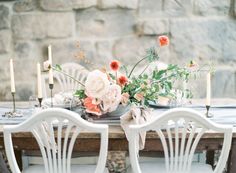 the table is set with white chairs and flowers on it, along with an arrangement of candles