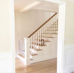 an open door leading to a white room with stairs and wood flooring in it