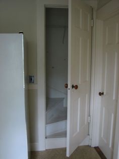 an empty room with two white doors and a refrigerator in the corner next to it