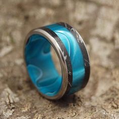 a ring with blue and black marble inlays sits on top of a rock