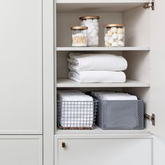 an organized closet with white linens, baskets and other items in gold lids on the shelves