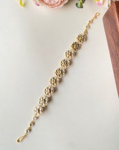 a close up of a bracelet on a table with flowers and a clock in the background