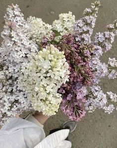 a person holding a bunch of flowers in their hand on the street with white gloves