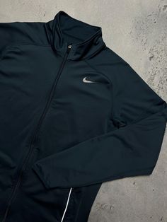 a black nike jacket laying on top of a cement floor next to a white wall