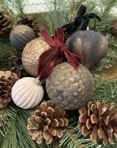 some ornaments are sitting on top of pine cones and fir branches with red ribbon around them