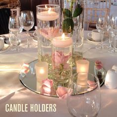 candles and flowers are placed in glass vases on a table with wine glasses around it