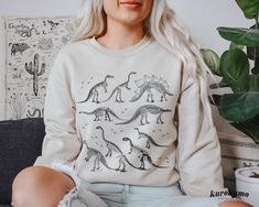 "Manifest the inner paleontologist in you with this sweater! This Unisex crewneck sweatshirt features an array of vintage dinosaur skeletons and footprints. It is perfect to style with different kinds of fashion like goblincore, dark academia, mall goth & more. Make sure to check out the other garment options below :) » O P T I O N S « ‣ Tshirt: https://www.etsy.com/listing/911118225 ‣ Hoodie: https://www.etsy.com/listing/1118755029 » A B O U T « ‣ This item is made to order using direct-to-garm Skeleton Sweater Green, Goblincore Grunge, Vintage Sweaters Skeleton, Academia Sweater, Dark Academia Sweater, Green Dinosaur Sweater, Skeleton Crewneck Sweater, Casual Dinosaur Print Crew Neck Sweatshirt, Dinosaur Sweatshirt