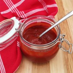 a jar filled with ketchup sitting on top of a wooden table next to a red towel