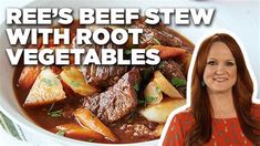 a woman standing in front of a bowl of stew with carrots, potatoes and beef