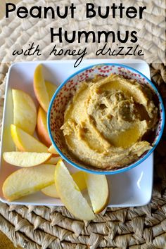 peanut butter hummus with honey dip in a blue bowl on a white plate next to sliced apples