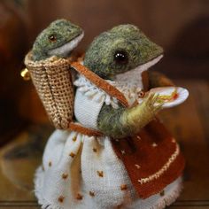 a small stuffed frog holding a plate and wearing a dress with an orange sash around its neck