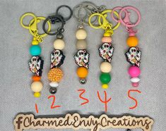 several key chains with charms attached to them on a white cloth covered surface, next to a wooden sign that says charmed my creations