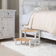 a white bed sitting next to a wooden dresser on top of a carpeted floor