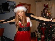 a woman dressed as santa clause dancing in front of a christmas tree with her arms stretched out