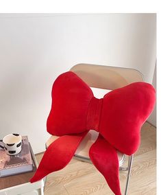 a red bow pillow sitting on top of a chair next to a coffee cup and book