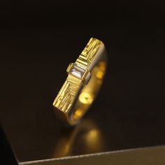 In architecture, axis marks the beginning of the plan distributing all parts of the building. The sleek Xyz axis diamond ring is inspired by both, modern architecture's geometrical elements and mineral structures. To balance against the minimalist order, Agata hand-carved diamond flanks to imitate growing crystals forming parallel stritations on its surface. Made in 18k gold, this intriguing ring stands out with its modern and dynamic aesthetics featuring a white diamond baguette. Perfect as an alternative engagement ring; ideal for mineral and architecture enthusiasts. Please note this ring is handmade and unique, so its texture may vary slightly from the one presented. Finer details: Material: 18k yellow gold. Measurements: 2.1 x 0.4 cm. Style: medium high profile, ornate front. Diamond: Growing Crystals, Diamond Baguette, Ring Stand, Alternative Engagement Rings, The Plan, Baguette Diamond, Modern Aesthetics, Bosnia And Herzegovina, White Diamond