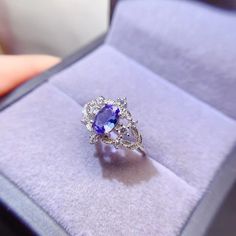 a ring with an oval shaped blue stone surrounded by small white diamonds in a velvet box