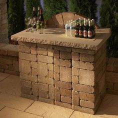 an outdoor bar with bottles and glasses sitting on it's back end, next to a brick wall