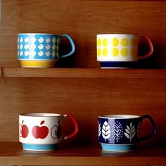 three colorful cups sitting on top of a wooden shelf