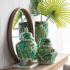 three green vases sitting on top of a wooden shelf next to a round mirror