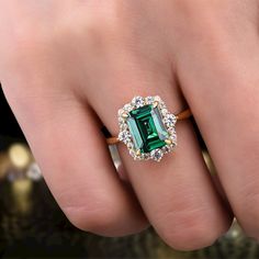 a woman's hand holding an emerald and diamond ring