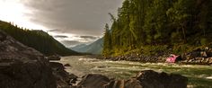 a river with rocks in the middle and trees on both sides, surrounded by mountains