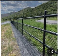 an image of a black fence on the side of a road with mountains in the background