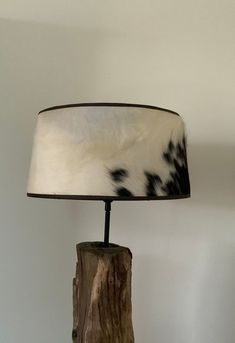 a lamp that is sitting on top of a wooden stump with a cowhide shade