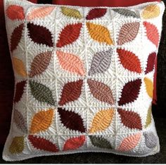 a crocheted pillow with colorful leaves on the front and back, sitting on a black couch