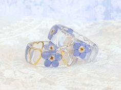 This is a lovely forget-me-not ring adorned with your choice of gold or silver harts.  Forget-me-nots symbolize true love and respect. When you give someone these tiny blooms, it represents a promise that you will always remember them and will keep them in your thoughts. They are also considered a symbol of fidelity and faithfulness. These make a great gift for your loved ones as well as family and friends.  Each piece in my shop is handmade by me. They are each unique and different, no piece can be recreated to be exactly the same as the previous. Every item is packed safely is a bubble wrap-lined envelope for safe postage. The ring is enclosed in a decorated tin for gifting. The creation of this ring is artisan made with silicone molds, sanded and polished by hand. Please consider that t Gold Rings With Pressed Flowers For Wedding, Adjustable Pressed Flowers Ring For Wedding, Forget Me Not Resin, Flower Wedding Band, Ring Flower, Promise Ring Gift, Flower Resin, Forget Me Nots, Losing A Loved One