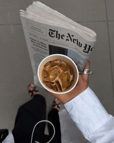 a person is holding up a newspaper and cup of tea