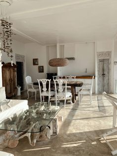 a living room filled with furniture and a glass dining table surrounded by white chairs on top of a hard wood floor