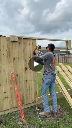 a man using a power drill on a wooden structure in the grass next to a fence