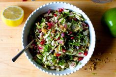 a white bowl filled with salad next to sliced lemons and lime wedges on a cutting board