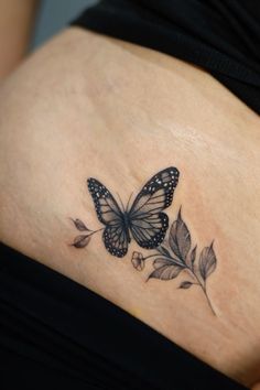 a woman's stomach with a butterfly and leaves tattoo on the side of her belly