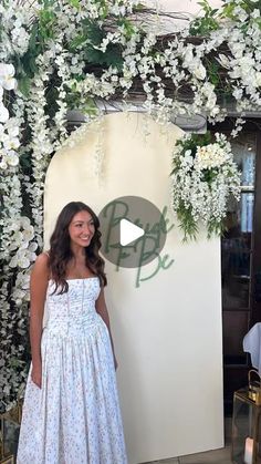 a woman standing in front of a flower covered wall