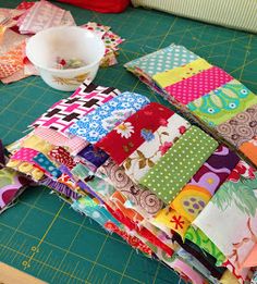 a cutting board topped with lots of different colored pieces of fabric next to a bowl