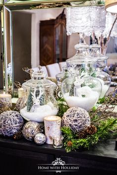 a table topped with lots of glass vases filled with christmas balls and greenery