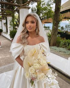 a woman in a wedding dress holding a bouquet of flowers and posing for the camera