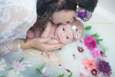 a woman holding a baby in her arms while laying on the ground next to flowers