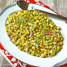 a white plate topped with corn salad next to a fork