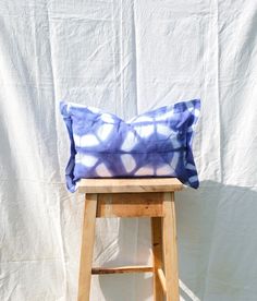 a blue and white pillow sitting on top of a wooden stool next to a white wall