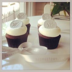 two cupcakes with white frosting and monogrammed decorations on them are sitting on a table