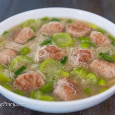 a white bowl filled with meatballs and green peppers on top of a wooden table