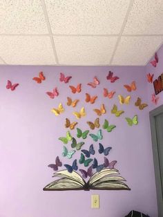 an open book sitting on top of a table in front of a purple wall with butterflies flying over it